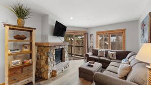 A cozy living room with a stone fireplace, wooden shelves, a comfortable sofa, and a TV mounted on the wall. - River Run Condo w/ Slope Views from Balcony, Walk To Gondola/Shops/Dining! (Keystone)