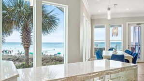 Eine moderne Küche mit einer großen Kochinsel, einem Essbereich mit blauen Stühlen und Blick auf den Strand.