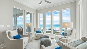 Ein geräumiges Wohnzimmer mit Meerblick, ausgestattet mit Deckenventilator, großen Fenstern und einer modernen Lampenleuchte.
