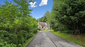 A residential street with a house at the end, surrounded by dense green foliage.