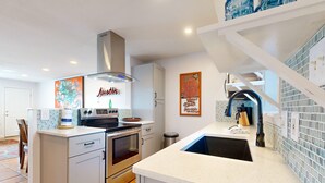 Een moderne keuken met witte kasten, een roestvrijstalen fornuis en een ingebouwde oven. Er is een witte aanrecht met een spoelbak en een achterwand van blauwe tegels.