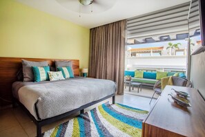 A hotel room with a bed, a desk, a chair, a balcony with a view, and a window with curtains.