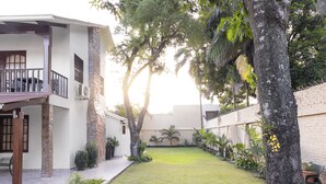 A courtyard with a lawn, a stone wall, and a building with a balcony. - Hotel BY Armonia SCZ (Santa Cruz)