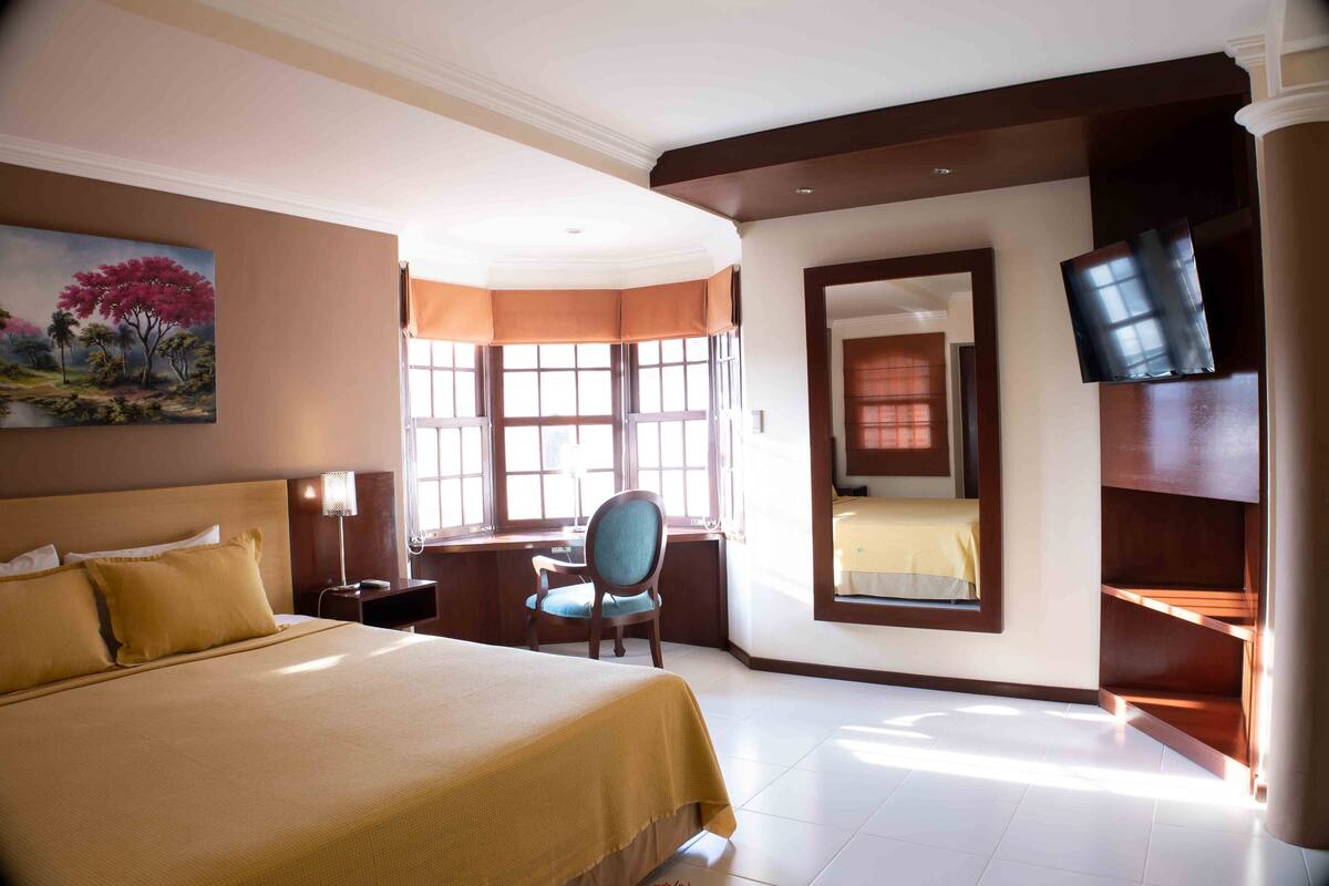 A hotel room with a large bed, a desk with a chair, a television, and a window with curtains.