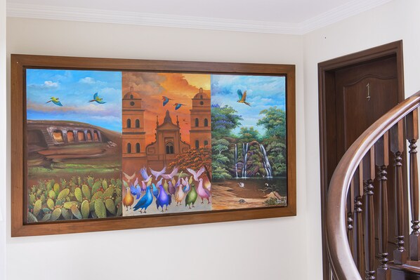 A large, framed mural depicting various scenes including birds, cacti, and a waterfall. - Hotel BY Armonia SCZ (Santa Cruz)