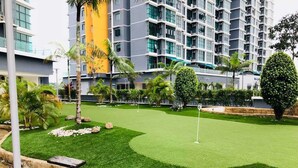 A well-maintained golf course with a putting green, surrounded by palm trees and modern buildings in the background. - Ilman's Loft@Vista Alam HILLVIEW-PS4-500MBPS (Shah Alam)