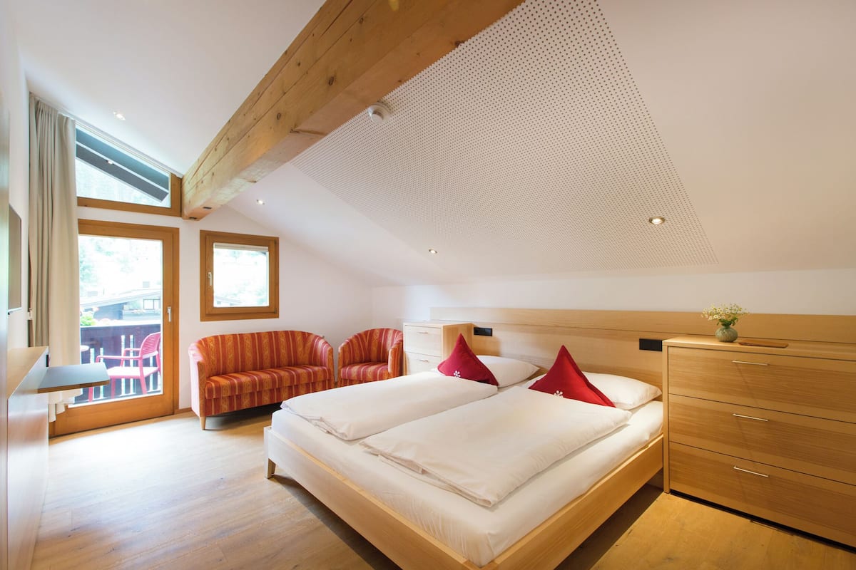 Un dormitorio con dos camas, un aparador de madera, un sofá y una zona de comedor con mesa y sillas.