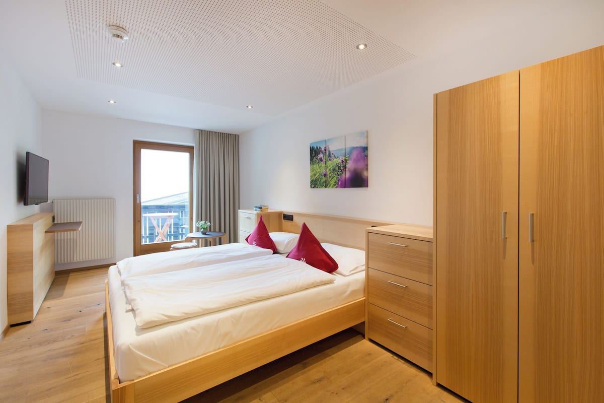 Una habitación de hotel moderna con una cama grande, un armario de madera y un televisor sobre un soporte.