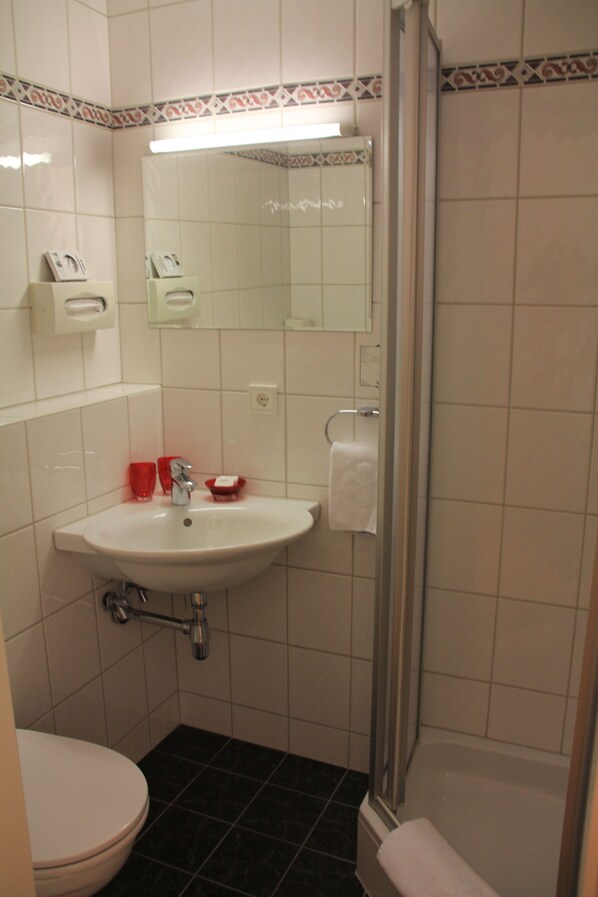 A bathroom with a white sink, a mirror, a glass shower enclosure, and a toilet. - Hotel Mateera (Sankt Gallenkirch)