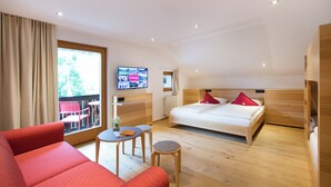 A modern hotel room with a large bed, a sofa, a small table, and a TV on the wall.