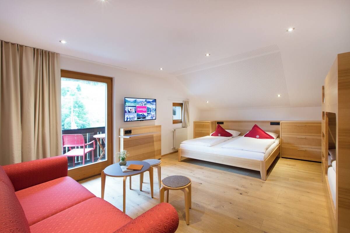 Una habitación de hotel moderna con una cama grande, un sofá, una mesita y un televisor en la pared.