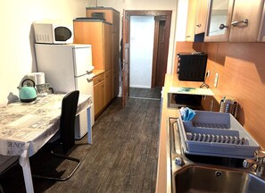 A compact kitchen with a microwave, refrigerator, sink, and a small dining area with a table and chair. - Sultanias Homesharing (Nuremberg)
