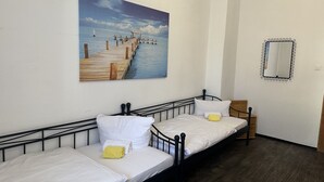 A room with two single beds, a wooden desk, a chair, a wall-mounted mirror, and a painting of a pier. - Sultanias Homesharing (Nuremberg)