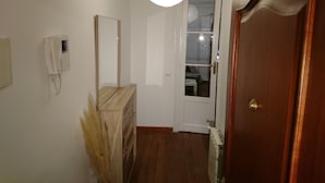 A hallway with a wooden dresser, a white phone, a mirror, a door, and a radiator. - Apartamentos Plaza Mayor (León)