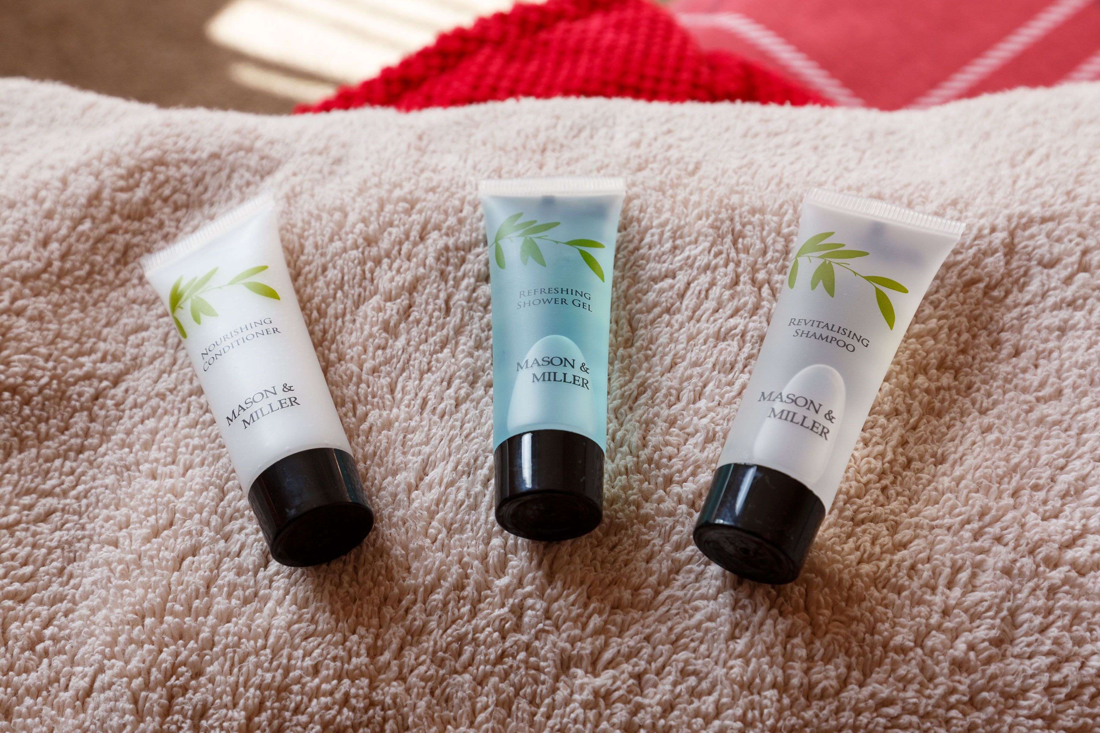 Three tubes of MASON & MILLER shower gel on a beige towel.