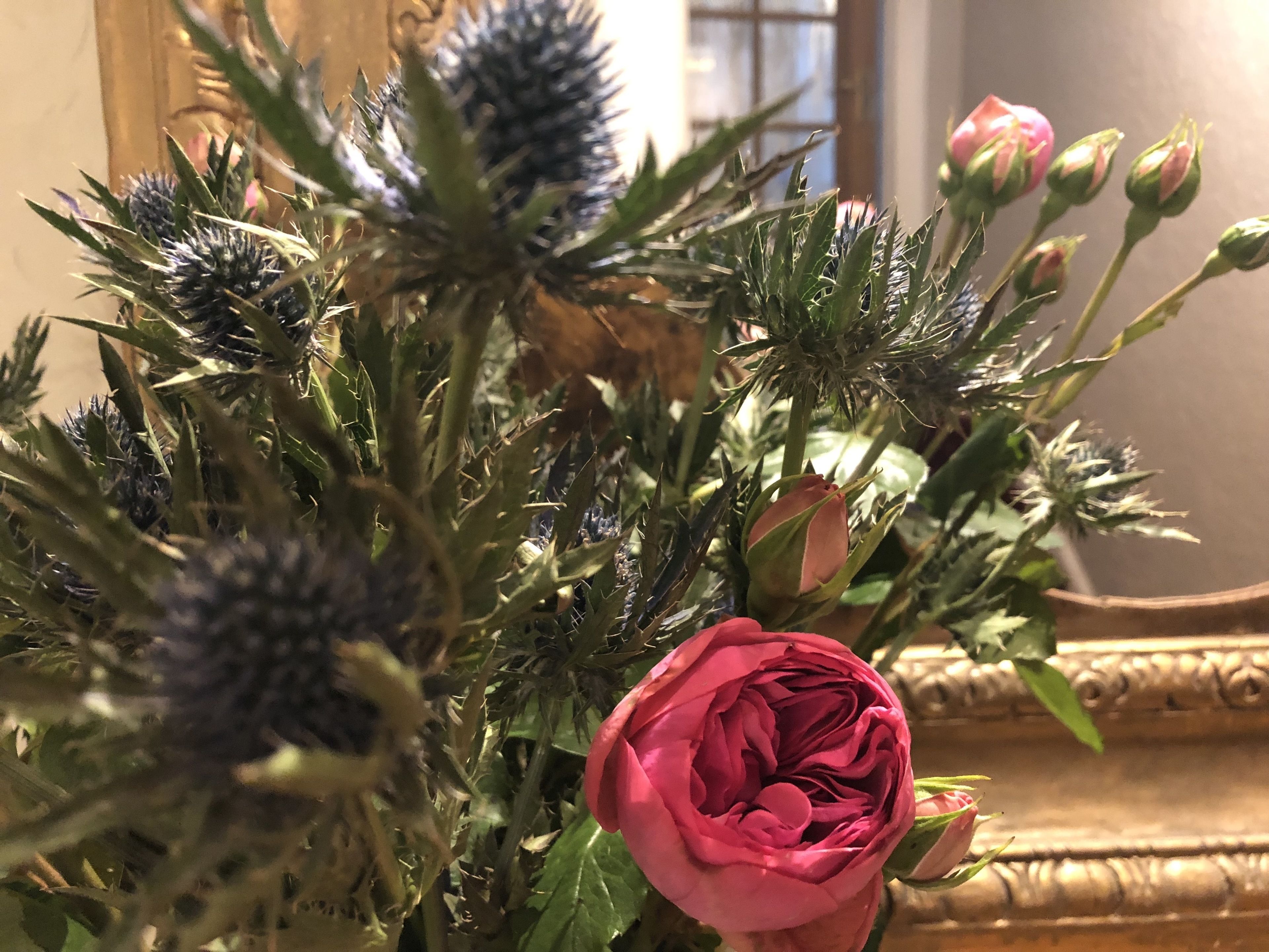 Un ramo de flores con una rosa rosa destacada, que incluye cardos y capullos, en un jarrón.