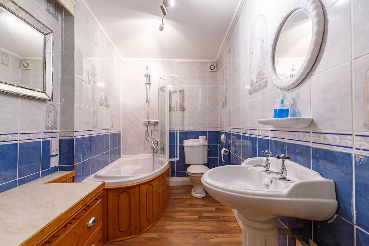 A bathroom with a bathtub, sink, and toilet, featuring blue and white tiles and wooden cabinets.