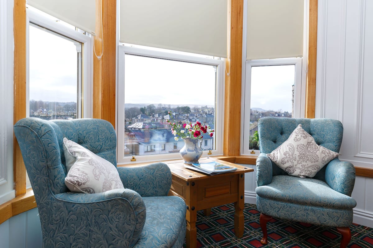 A room with two blue armchairs, a wooden table, and a vase with flowers.