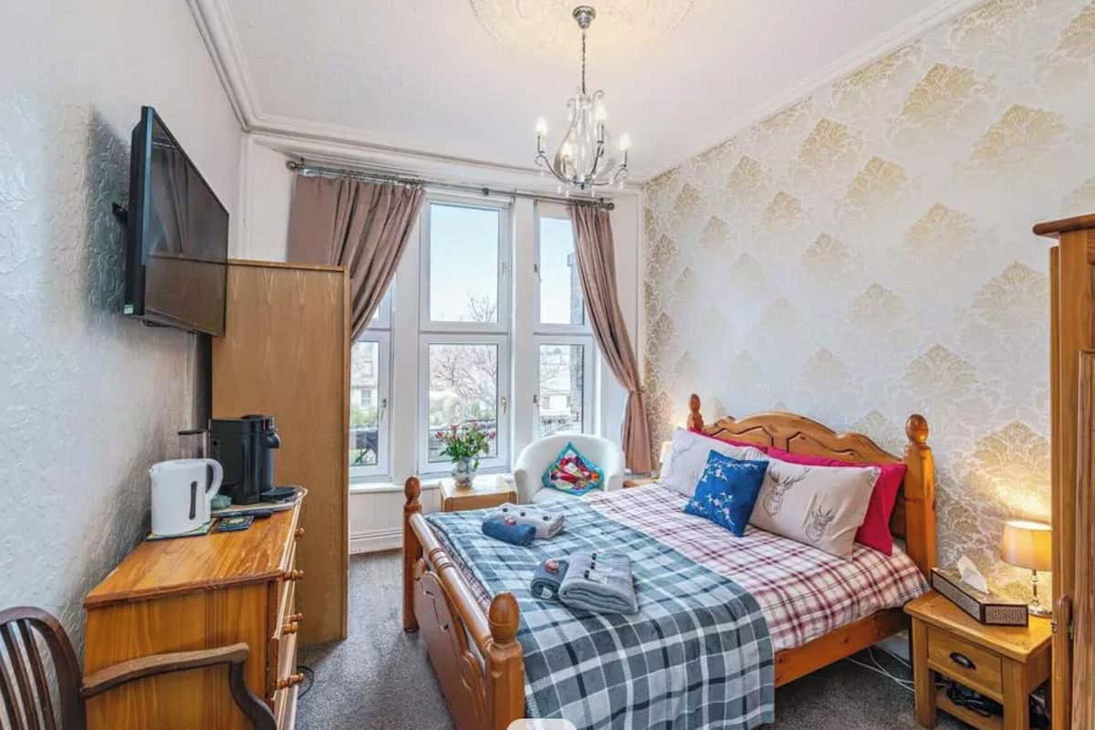 A bedroom with a bed, bedside table, chair, desk, and a TV mounted on the wall.