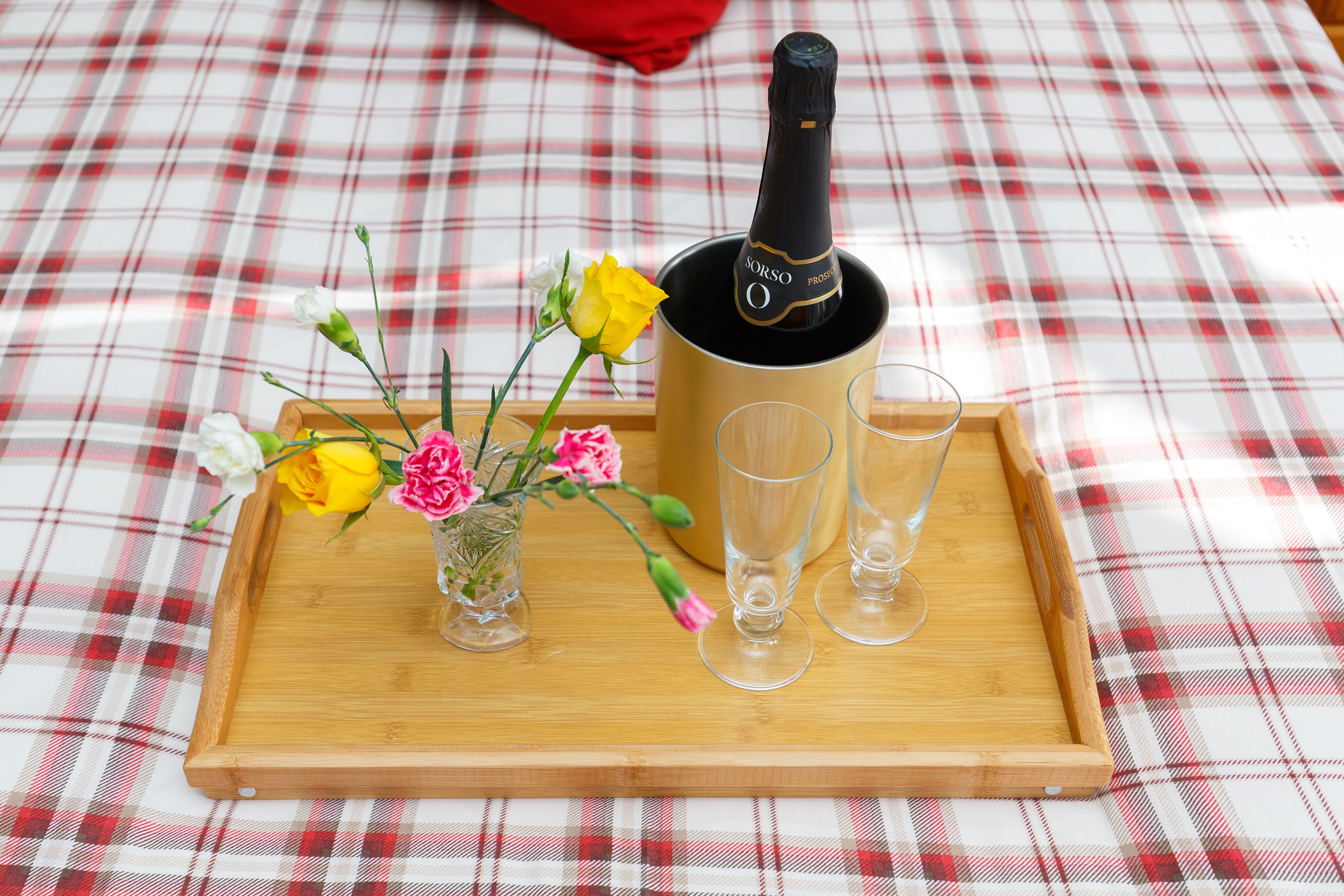 Une bouteille de Prosecco SORSO, deux verres et un petit vase avec des fleurs, le tout posé sur un plateau en bois.
