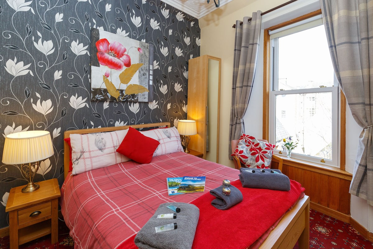 A neatly made bed with a red and white checkered bedspread, a red pillow, and a book titled "The Secret of the Island".