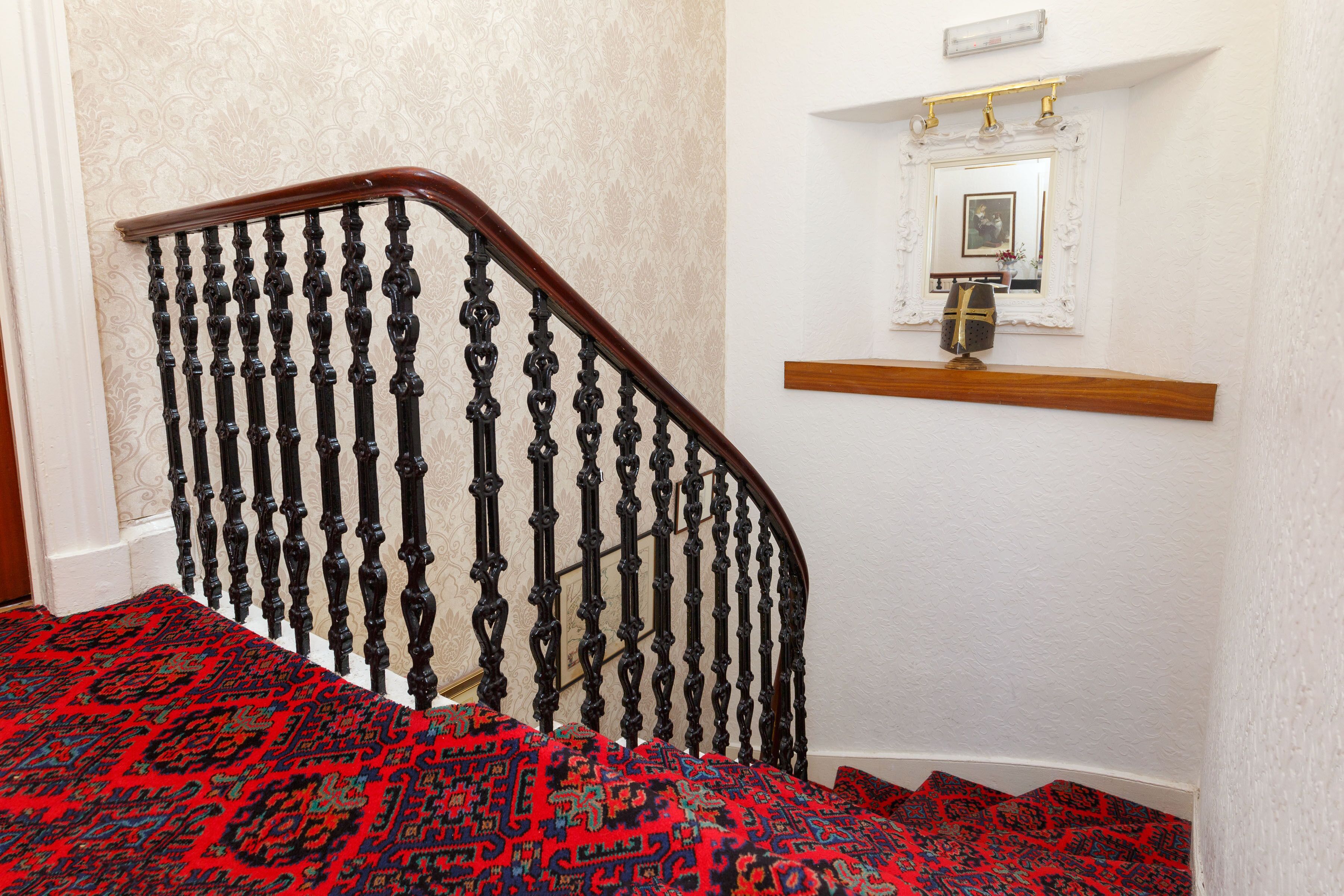 Una escalera con barandillas negras ornamentadas y un tapete rojo estampado.