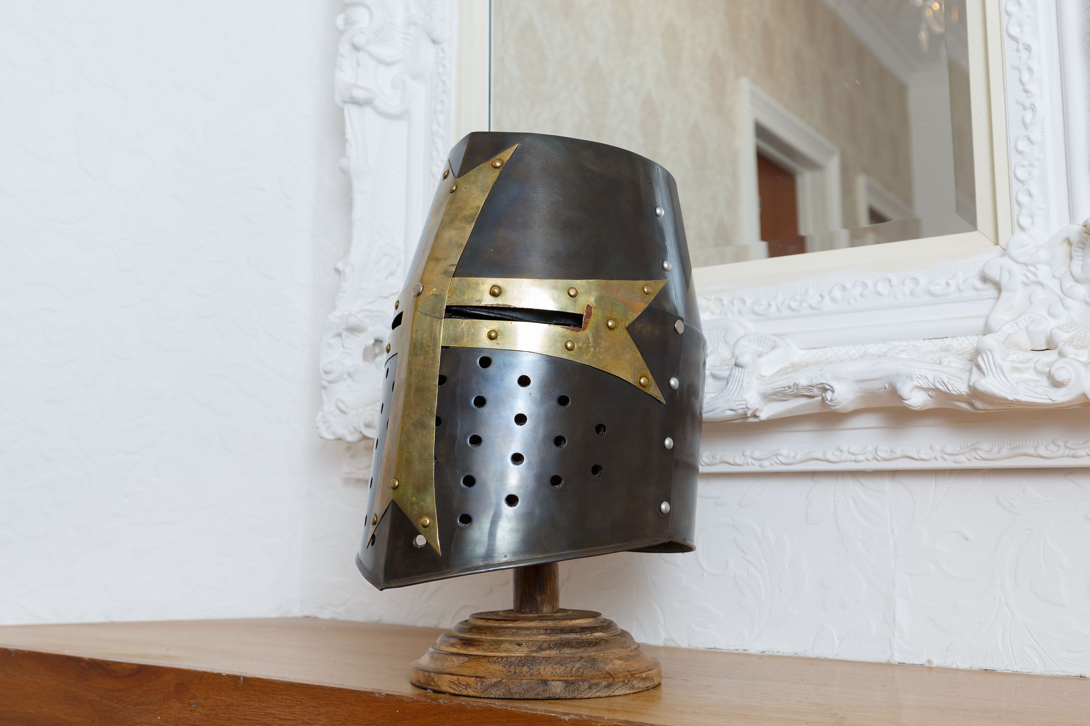 Un elmetto medievale su un supporto in legno, con uno specchio su uno sfondo bianco.