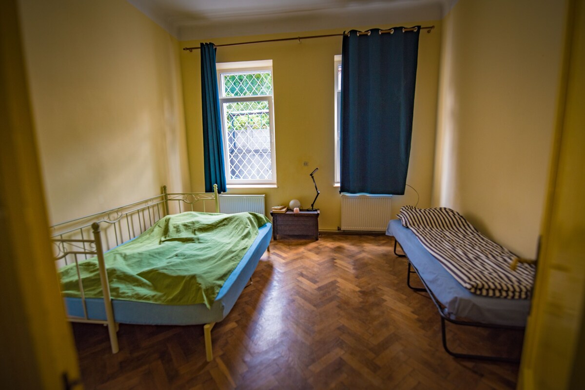 A room with a bed, a bench, a radiator, and a window with curtains.