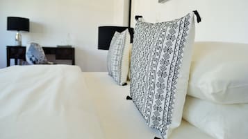 A neatly made bed with white linens and a patterned throw blanket, a bedside table with a lamp, and a chair in a hotel room.