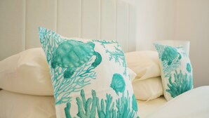 Un lit avec une literie blanche et des oreillers à motifs corail et turquoise.