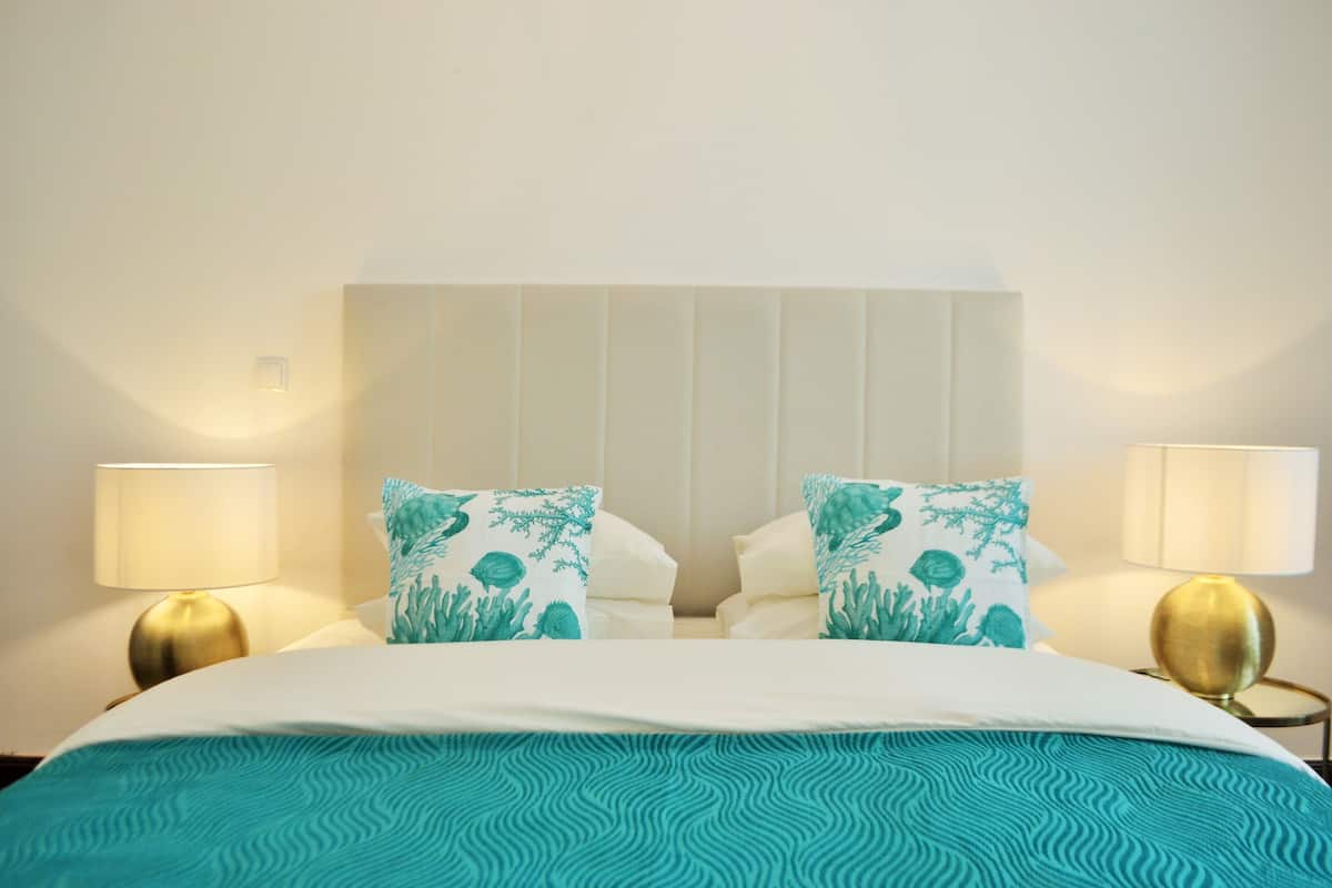Una habitación de hotel con una cama grande, dos almohadas con diseño marino y dos lámparas de noche.