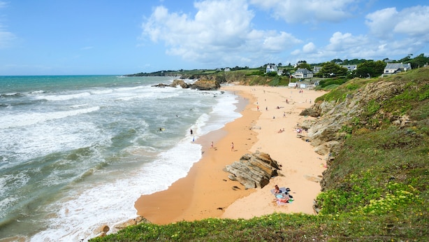 Une plage bordée de falaises rocheuses, avec une étendue de sable et des maisons le long de la côte.