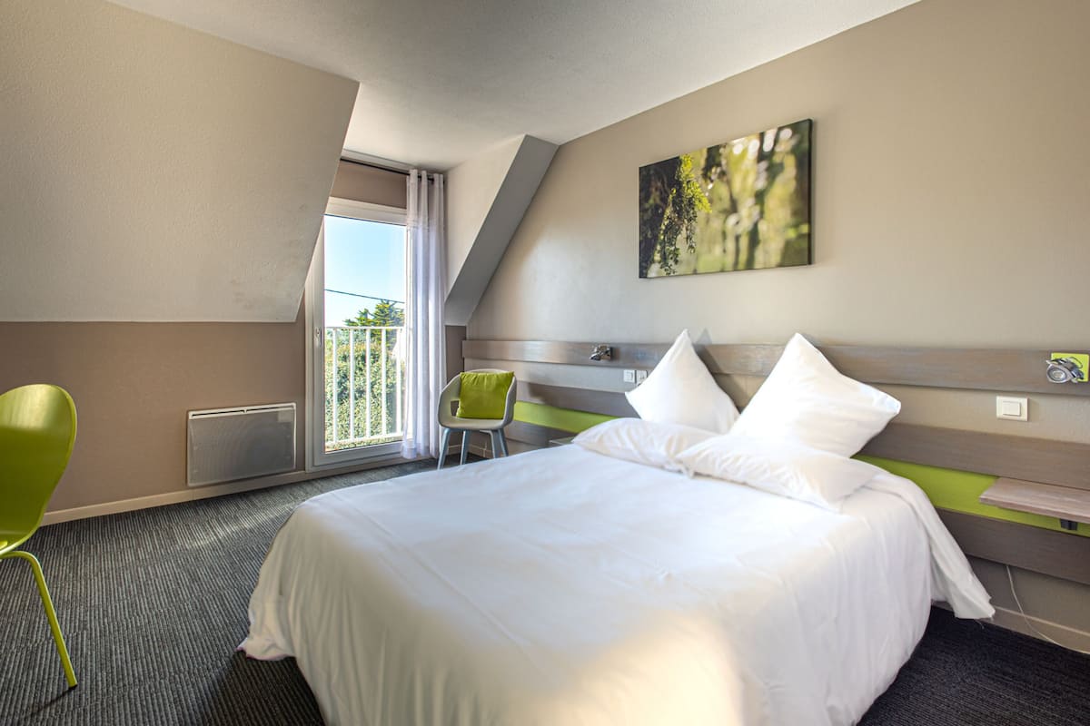 Une chambre d’hôtel avec un grand lit, une chaise, une fenêtre donnant sur un beau paysage et un tableau accroché au mur.