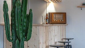 Un coin bar avec des lambris en bois, un cactus, une radio ancienne et trois tabourets.