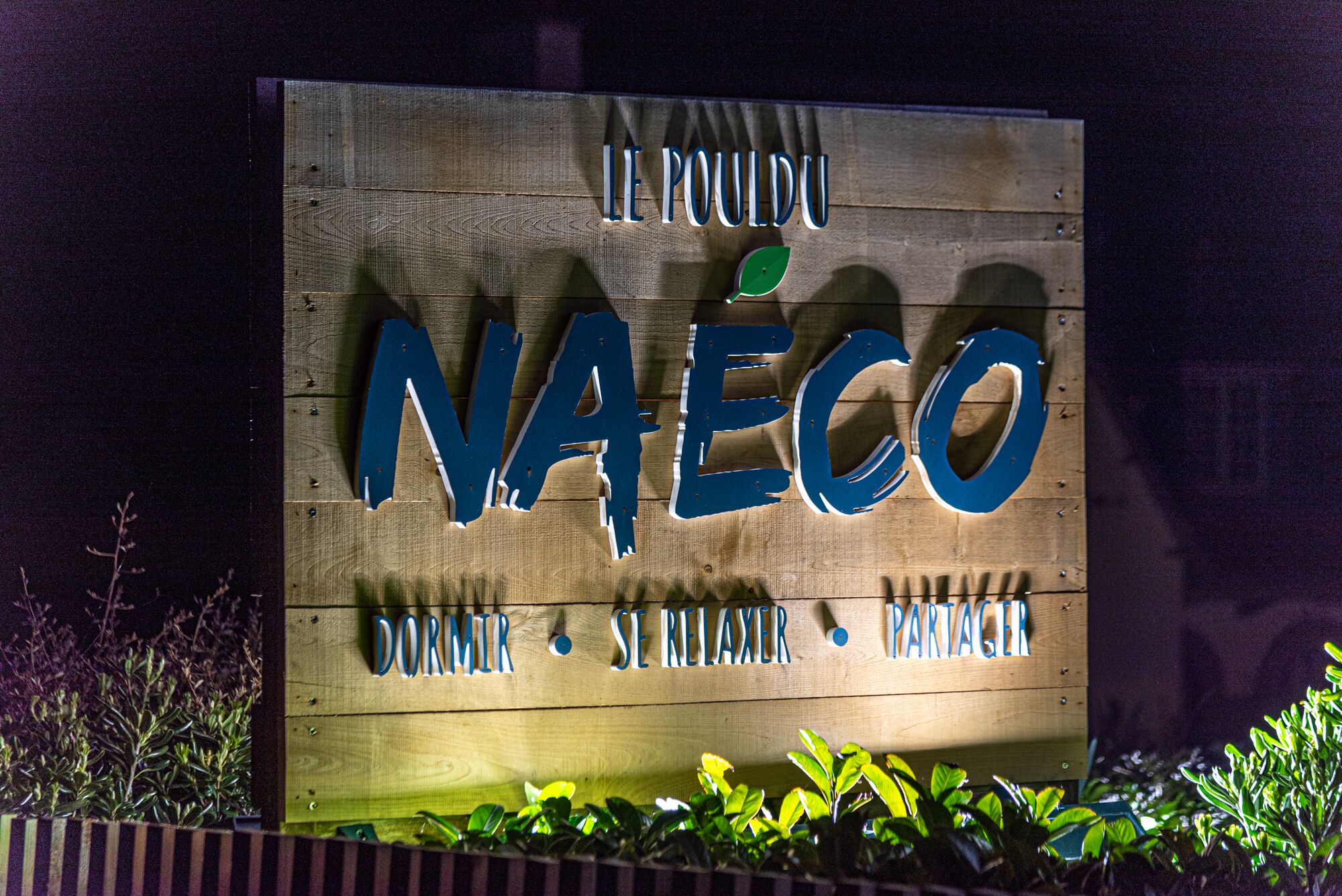 Un letrero de madera con las palabras "NAECO" y "DORMIR SE RELAXER PARTAGER", que indica un hotel o casa de huéspedes.