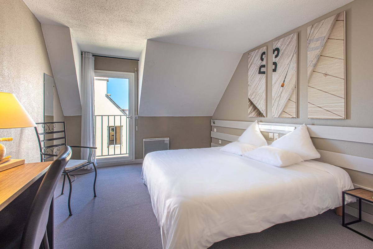 Une chambre d’hôtel avec un grand lit, un bureau avec une chaise, une fenêtre avec des rideaux et une vue sur l’extérieur.