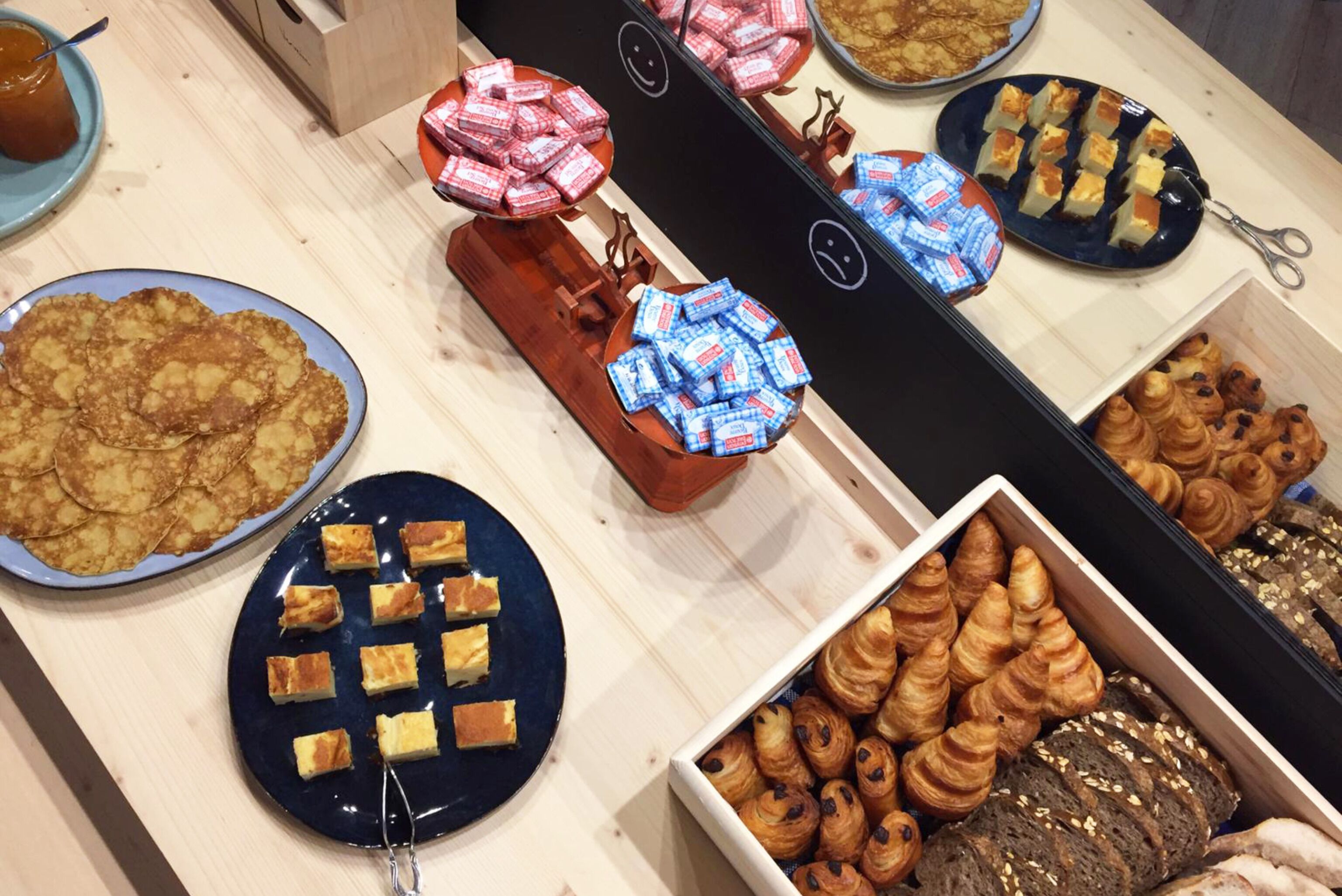 A buffet table with various pastries, including croissants and cakes, arranged on plates and in a box.