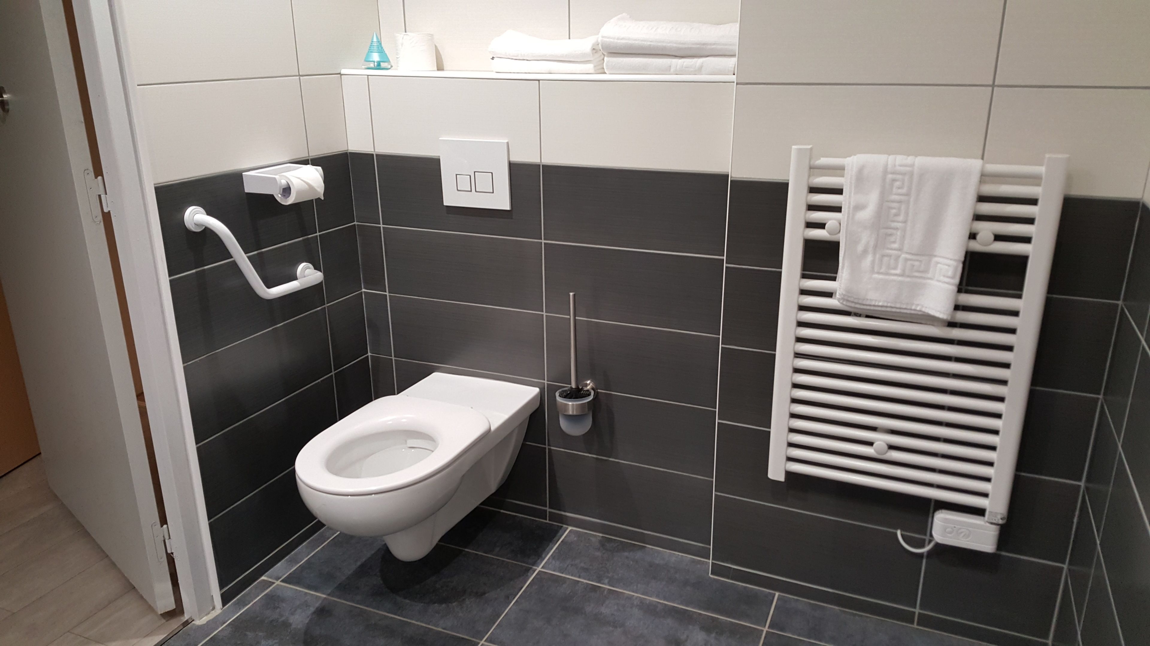 Une salle de bain moderne équipée de toilettes, d’un sèche-mains, d’un porte-serviettes et d’un support à papier toilette.