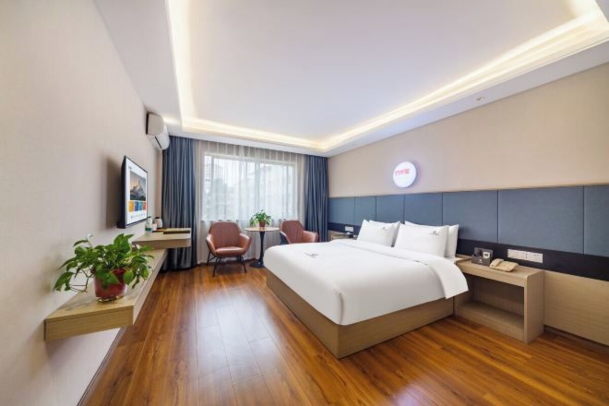 Quarto de hotel moderno com uma cama grande, mesas de cabeceira, escrivaninha e uma cadeira.