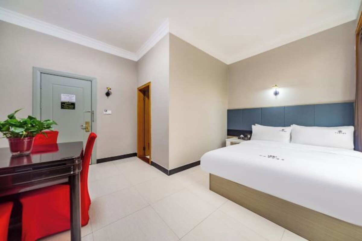 Quarto de hotel com cama, escrivaninha, cadeira e planta em vaso.