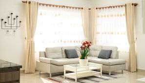 A modern living room with a beige sofa, a glass coffee table, and a decorative plant. - Melbourne Residence (Siem Reap)