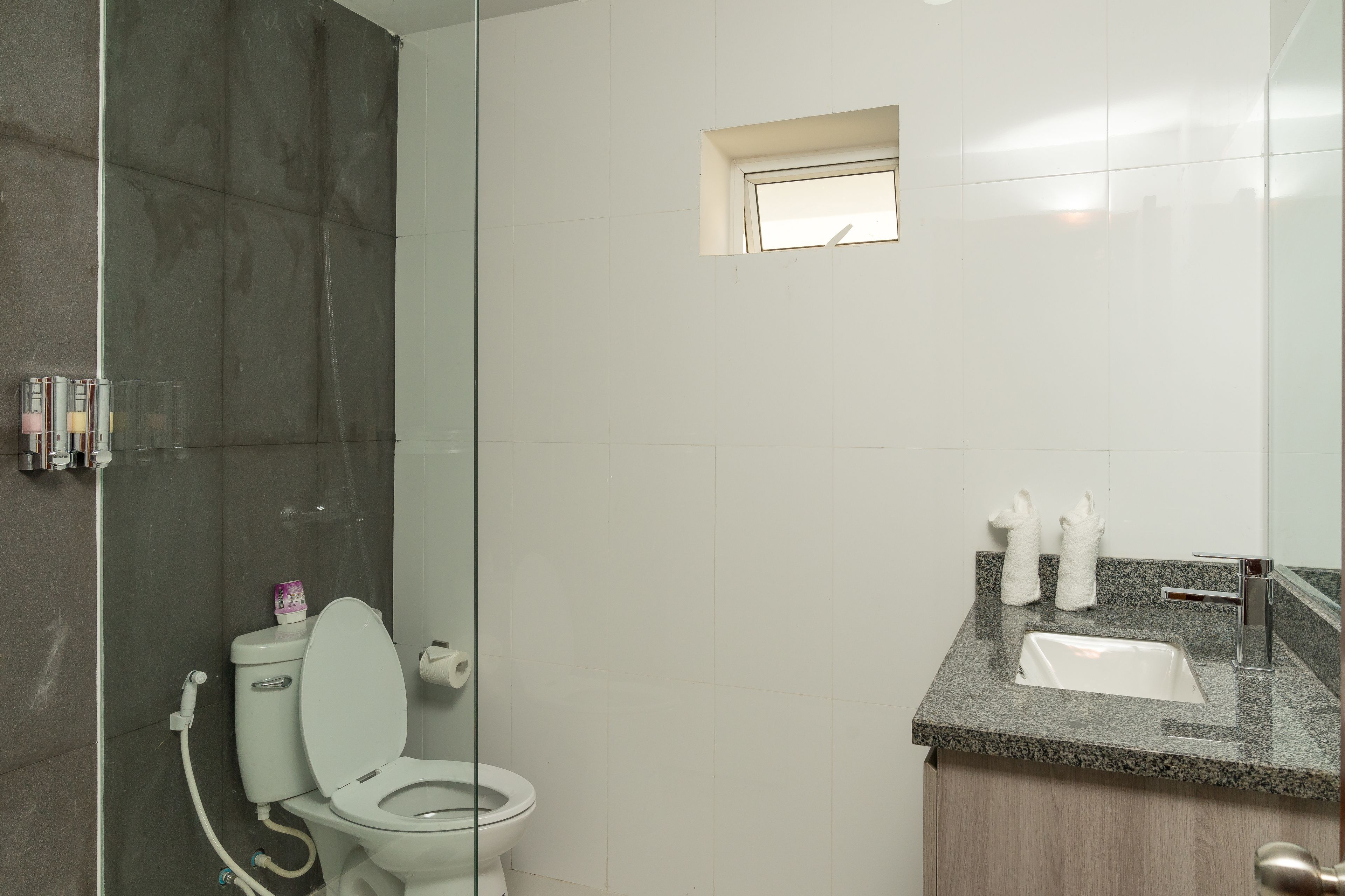 A modern bathroom with a glass-enclosed shower, a white toilet, and a granite countertop with a sink and towel rack.