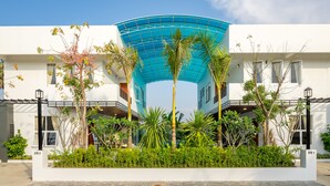 A modern building with a curved blue roof, surrounded by lush greenery and palm trees. - Melbourne Residence (Siem Reap)