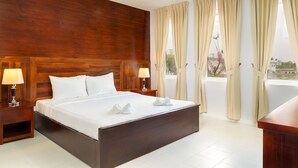 A hotel room with a wooden headboard, a large bed with white linens, two bedside lamps, and beige curtains. - Melbourne Residence (Siem Reap)