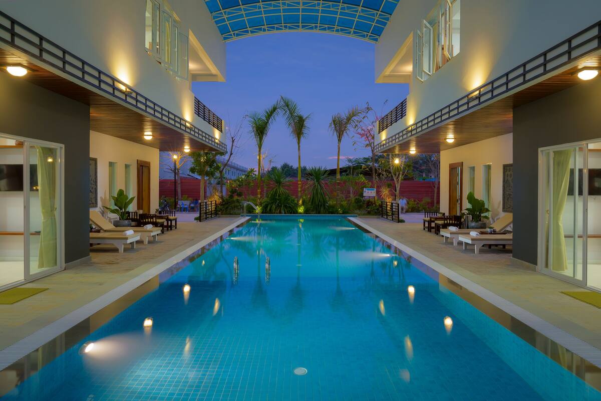 A swimming pool with lounge chairs and a covered area, surrounded by plants and a clear sky.