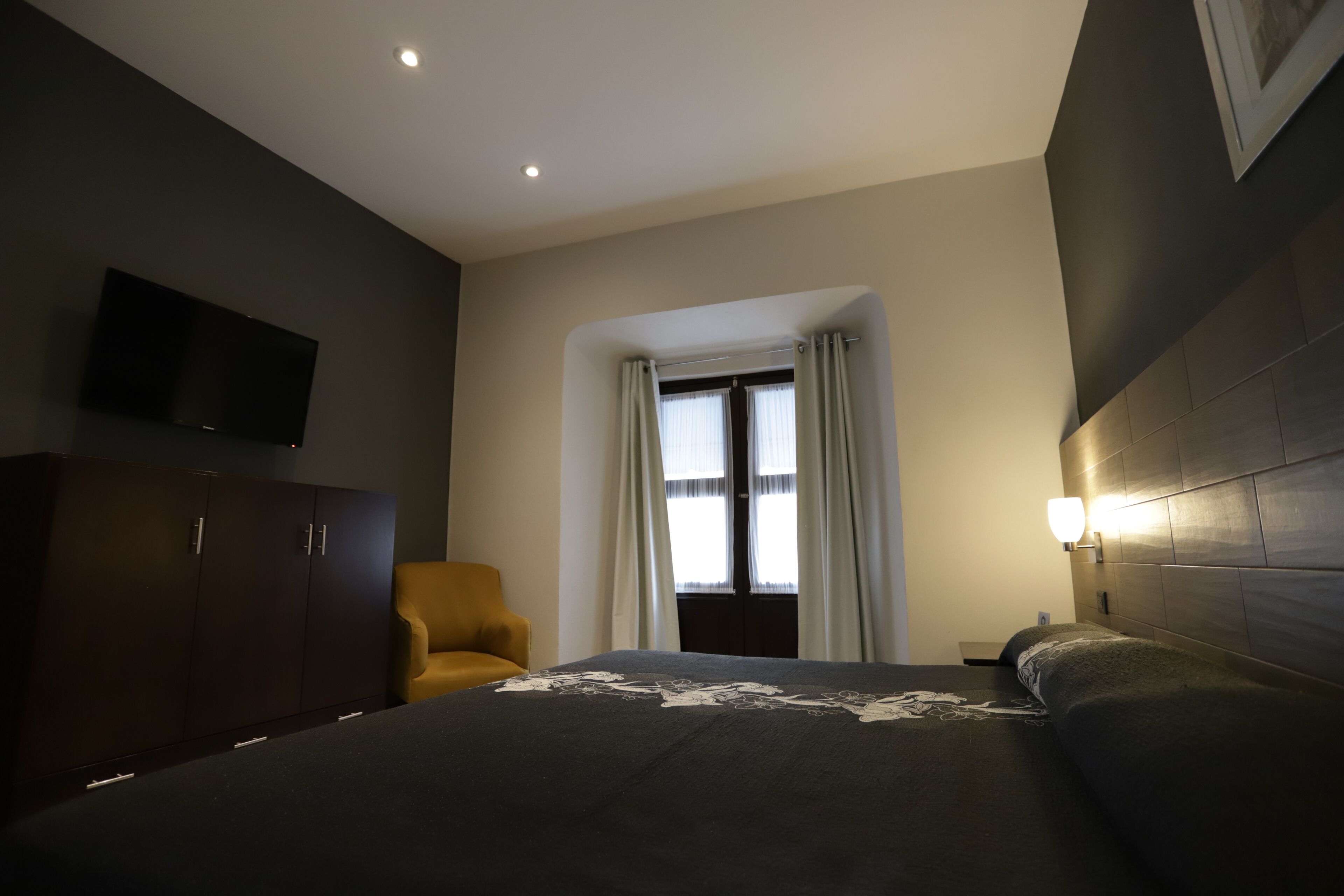 A modern hotel room with a large bed, a wardrobe, a television, and a window with curtains.