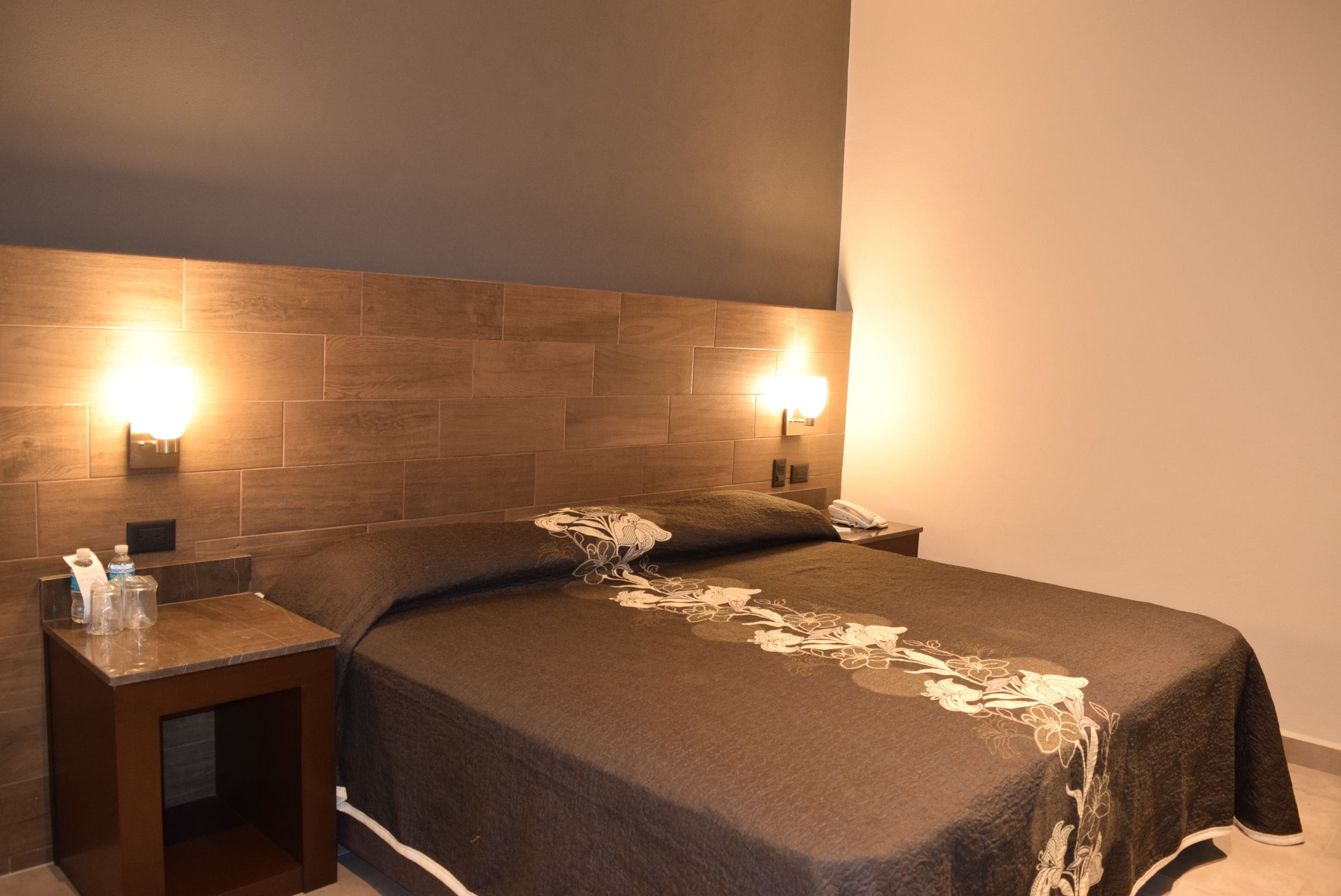 Une chambre d’hôtel avec un grand lit, deux tables de chevet et des lampes fixées au mur.