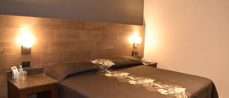 Une chambre d’hôtel avec un grand lit, deux tables de chevet et des lampes fixées au mur.