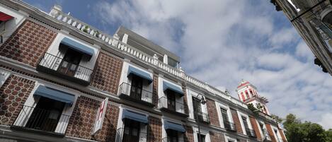 Un edificio de varios pisos con fachada ornamentada, balcones con barandillas y una torre roja y blanca al fondo.