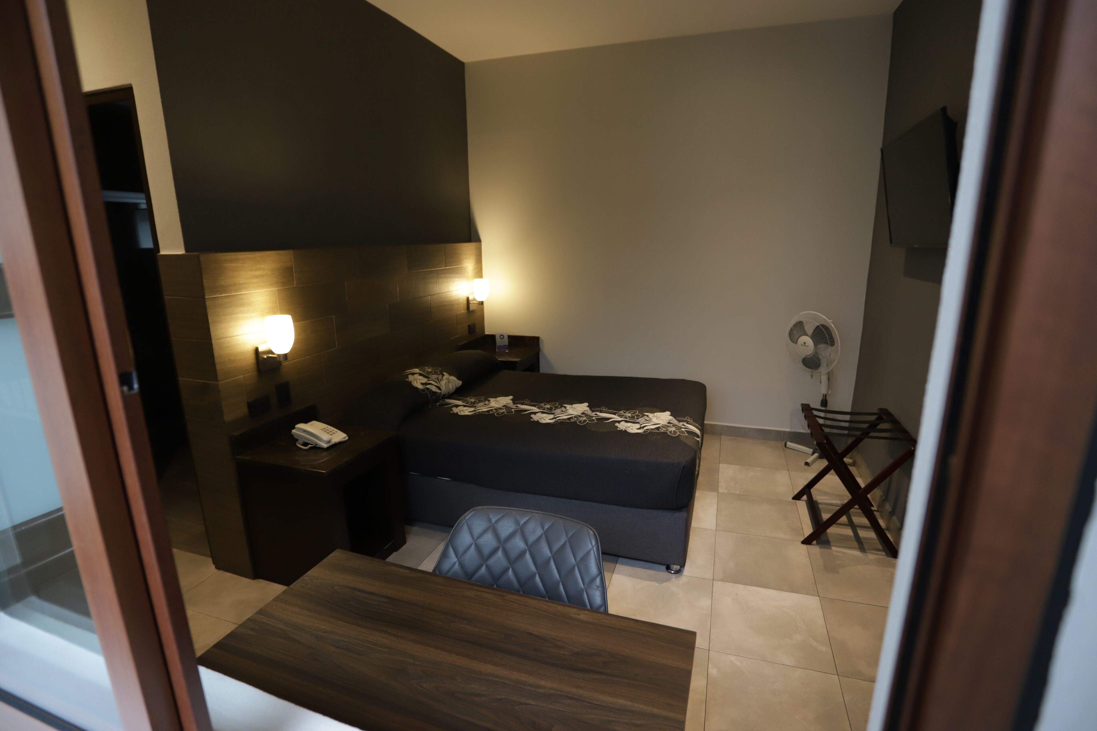 A hotel room with a bed, bedside tables, a desk, and a chair.